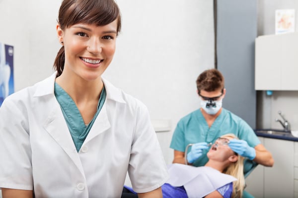 A dental assistant is smiling while a dentist works on a patient