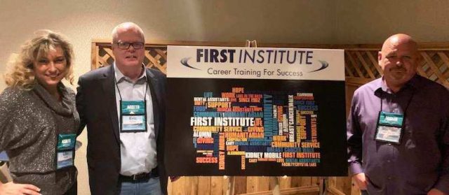 3 adults pose in front of a first institute sign