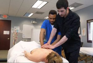 Two male massage therapist students giving a woman a massage